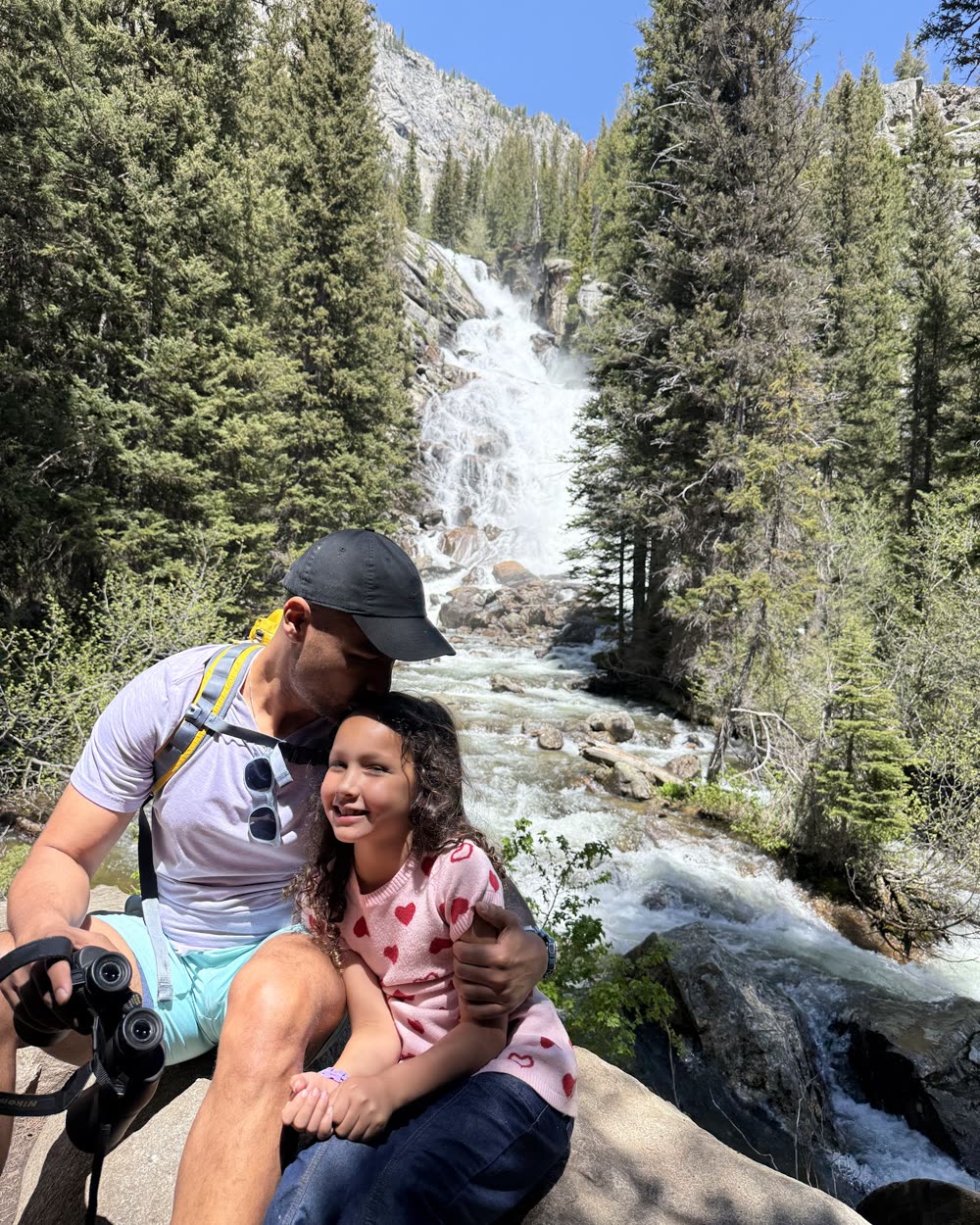 Sid with his daughter on a hike, a waterfall behind them